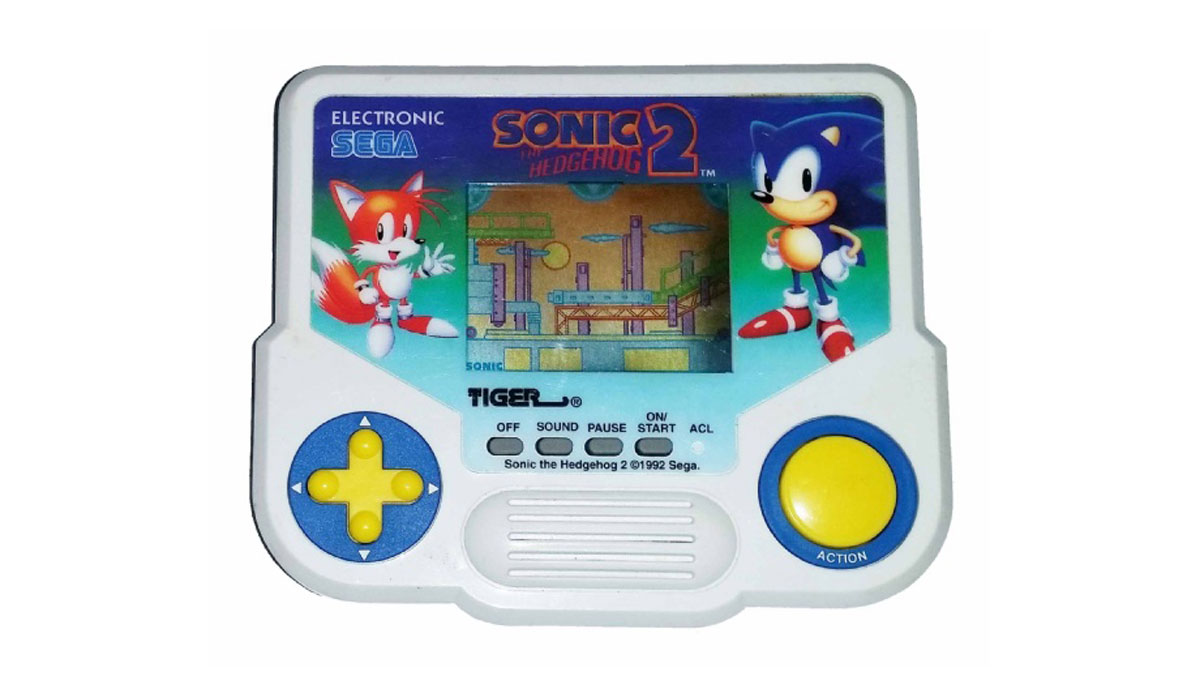 An electronic handheld game featuring Sonic the Hedgehog 2 by Sega. The device has classic Sonic characters on the front, with a small screen displaying game graphics. It includes yellow and blue controls for gameplay.