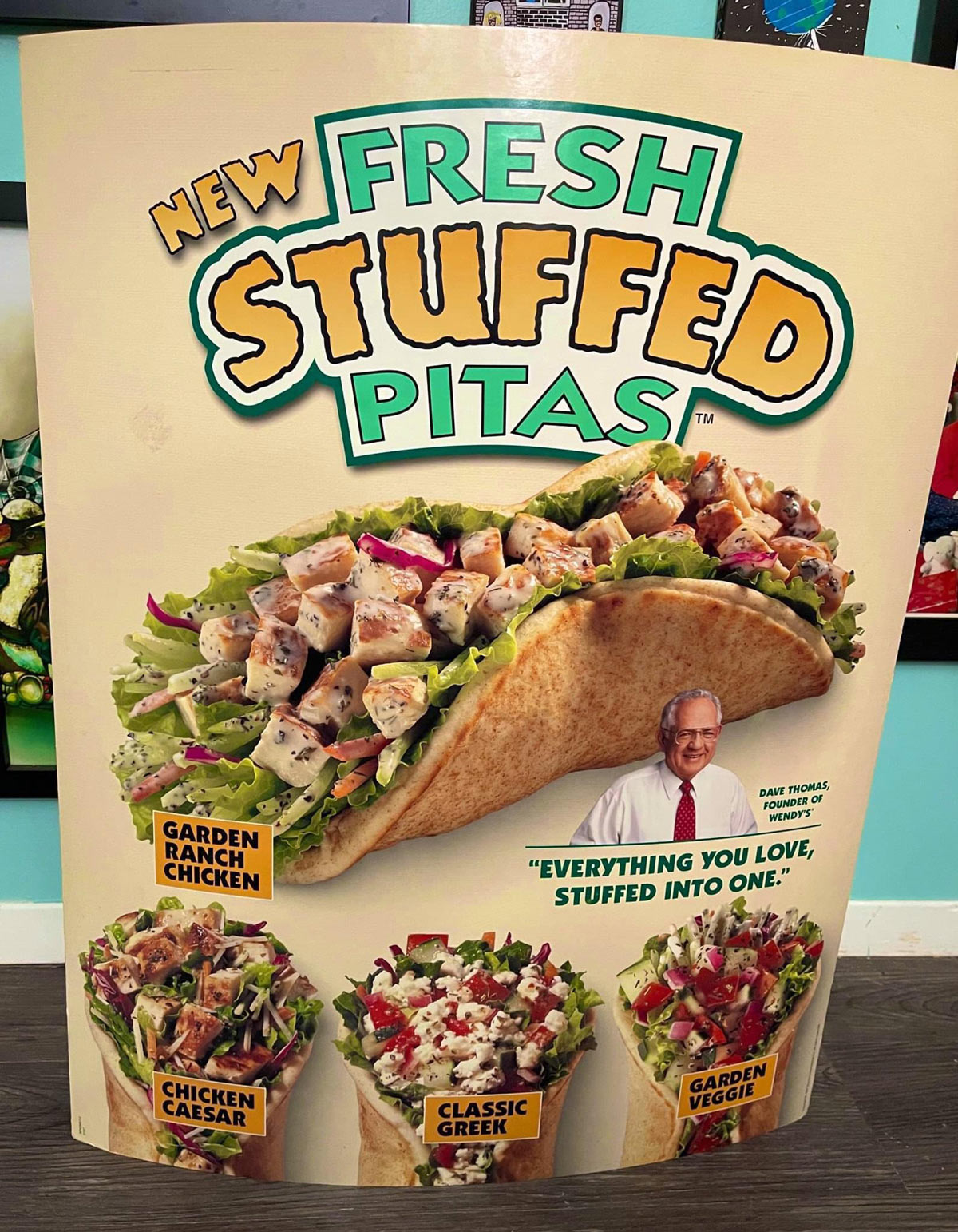 A colorful poster advertising Fresh Stuffed Pitas with images of four pitas: Garden Ranch Chicken, Chicken Caesar, Classic Greek, and Garden Veggie. A smiling man is pictured with the quote, Everything you love, stuffed into one.