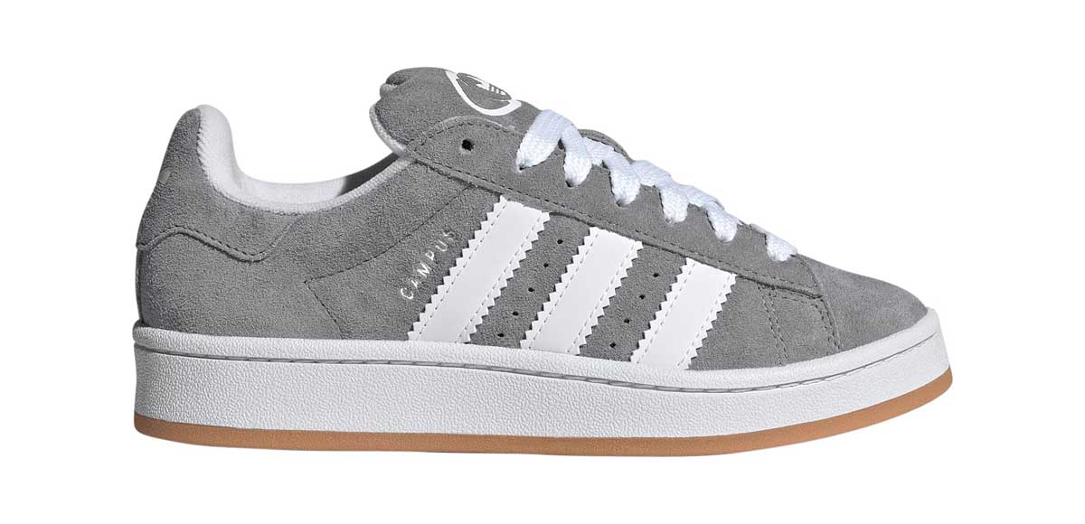 A gray suede sneaker with white laces, white leather stripes on the side, a white sole, and a light brown rubber outsole. The shoe features a low-top design and athletic style.