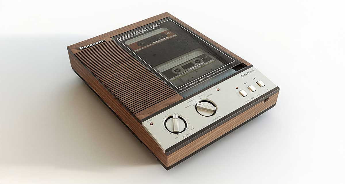 A vintage Panasonic cassette tape recorder with a wood finish, two large dials, three white buttons, and a cassette visible through a clear window on top.