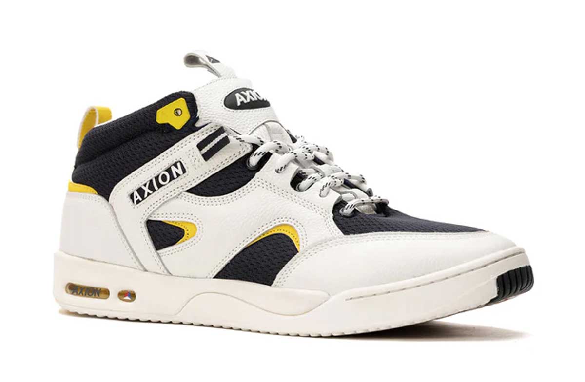 A white, black, and yellow mid-top sneaker with AXIOM branding, mesh and leather panels, yellow accents, and a white rubber sole, shown against a white background.