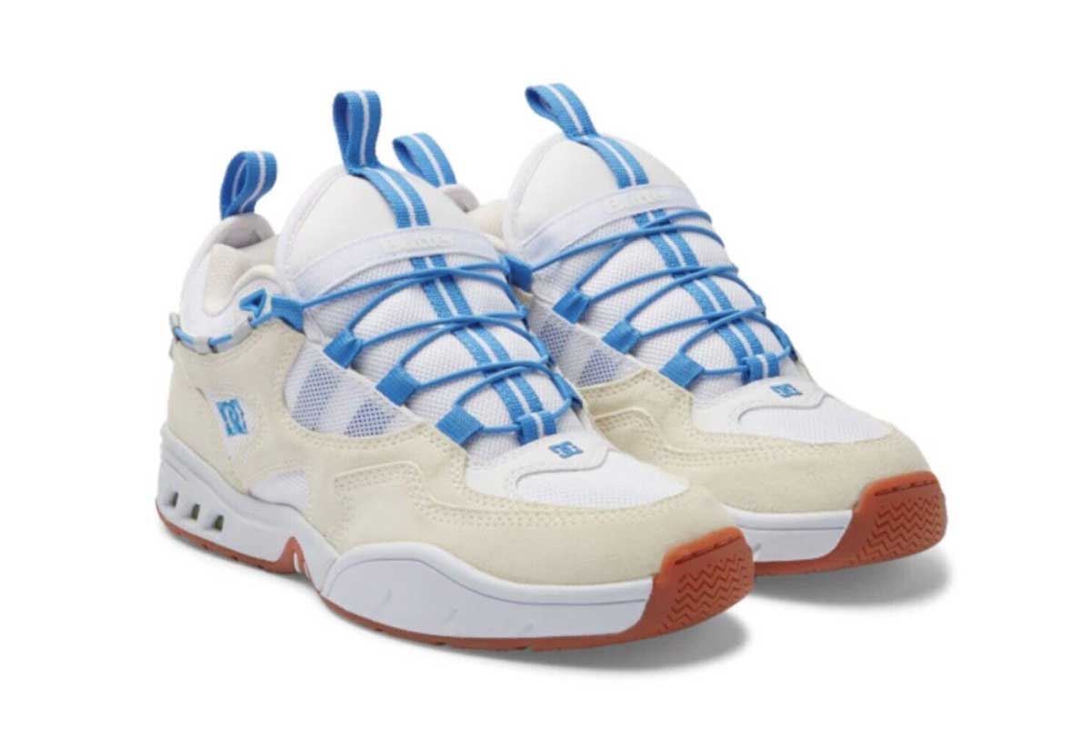 A pair of white and beige sneakers with blue laces and accents, mesh uppers, suede overlays, and brown rubber outsoles. The shoes feature a chunky design with pull tabs on the tongue and heel.