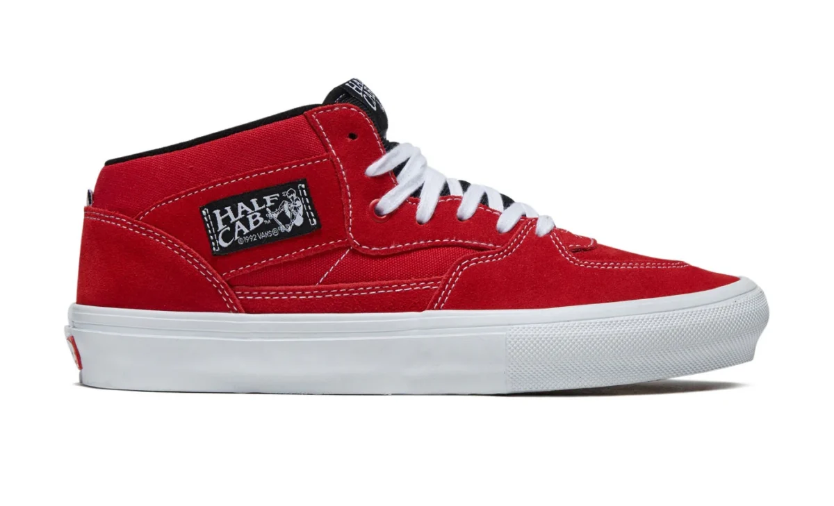A red suede skate shoe with white laces, a white sole, black collar, and a “Half Cab” patch on the side near the ankle. The shoe is viewed from the side on a white background.