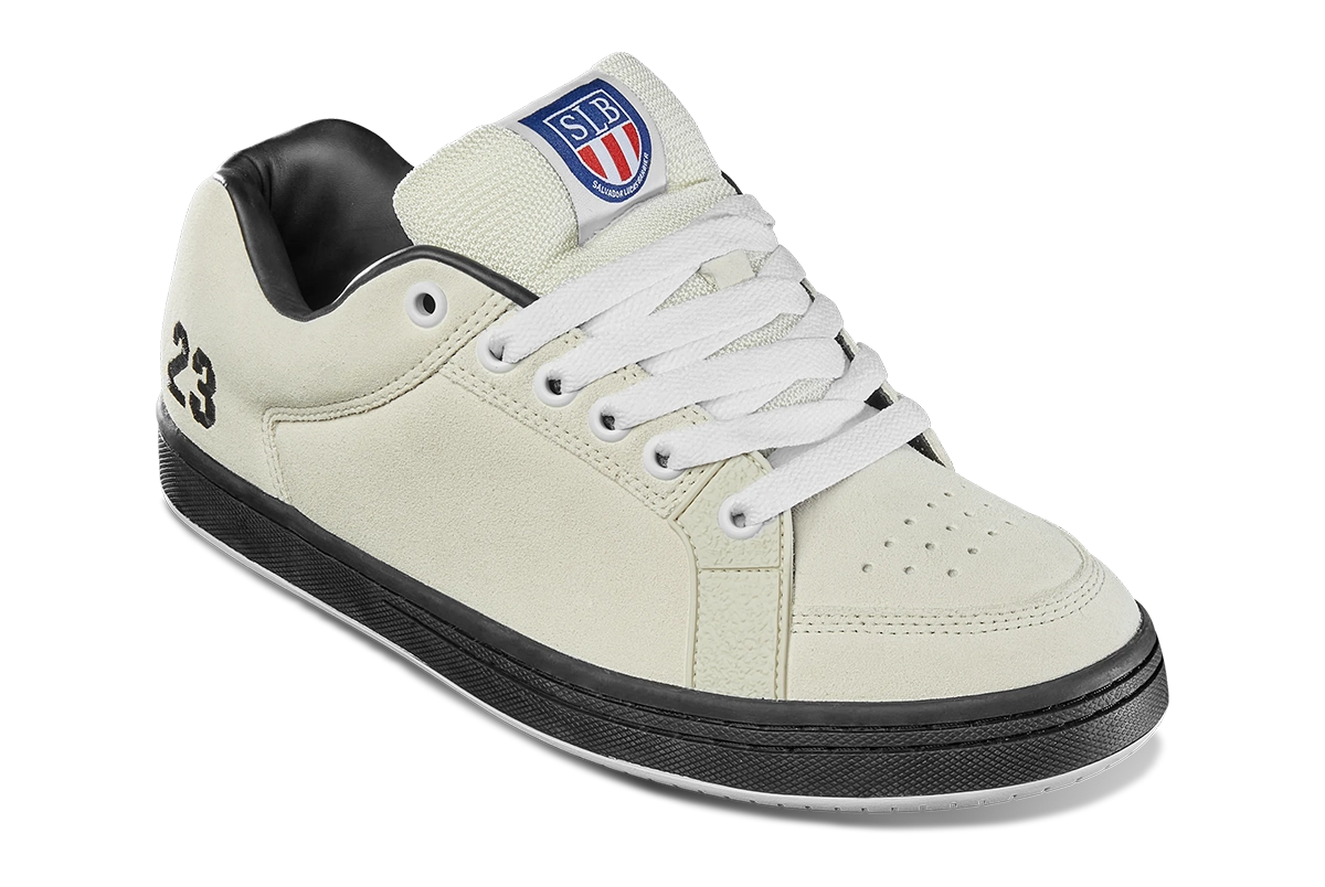 A cream-colored sneaker with white laces, a black sole, and black lining. The number 23 is on the heel, and a shield-shaped SB logo with red and blue details is on the tongue.