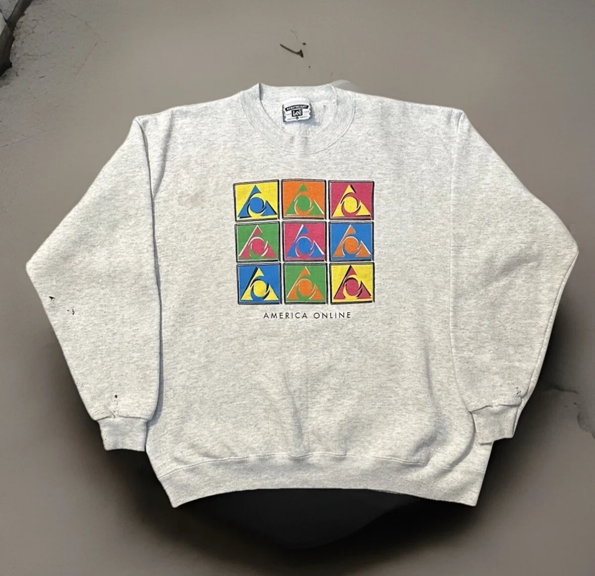 A gray sweatshirt features a colorful grid of twelve America Online (AOL) logos in various colors on the front, with AMERICA ONLINE printed below the design.