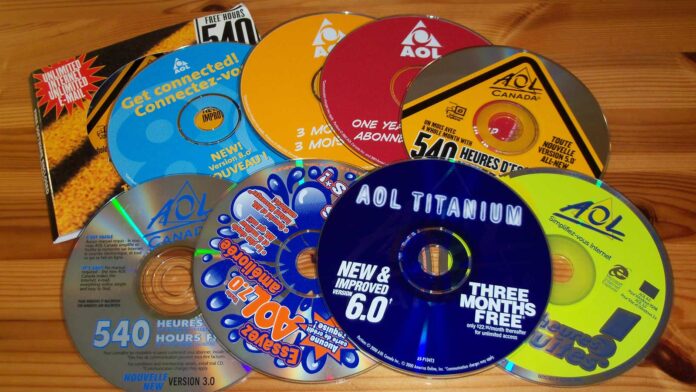 A collection of colorful AOL installation CDs and discs offering free trial hours is spread out on a wooden surface. The discs feature bold text with offers like “540 hours free” and “three months free.”.