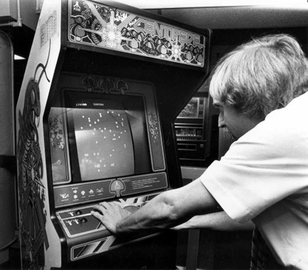 A person intently plays the classic arcade game Centipede, focusing on the screen and using both hands to control the game on an upright arcade cabinet.