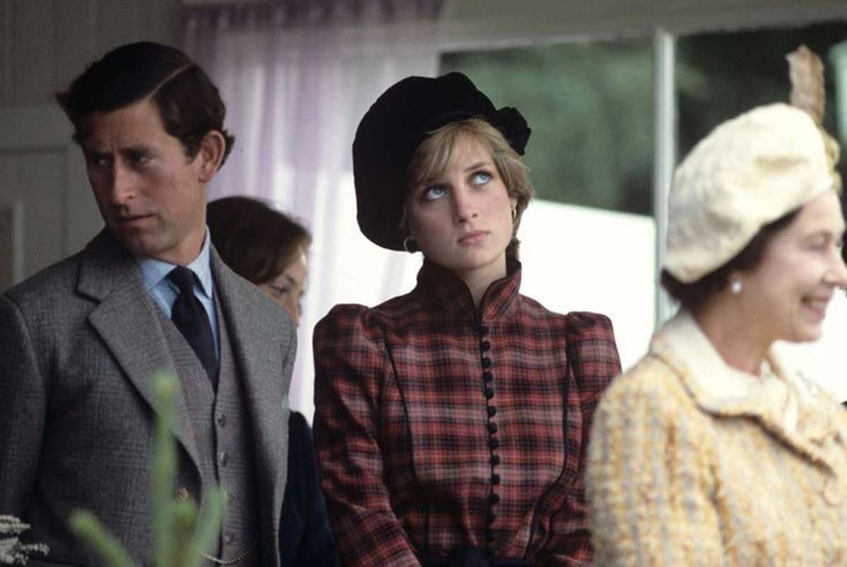 A woman in a plaid dress and black hat rolls her eyes while standing next to a man in a suit; another woman in a yellow outfit and hat is in the foreground, smiling. The setting appears to be indoors with light coming through windows.