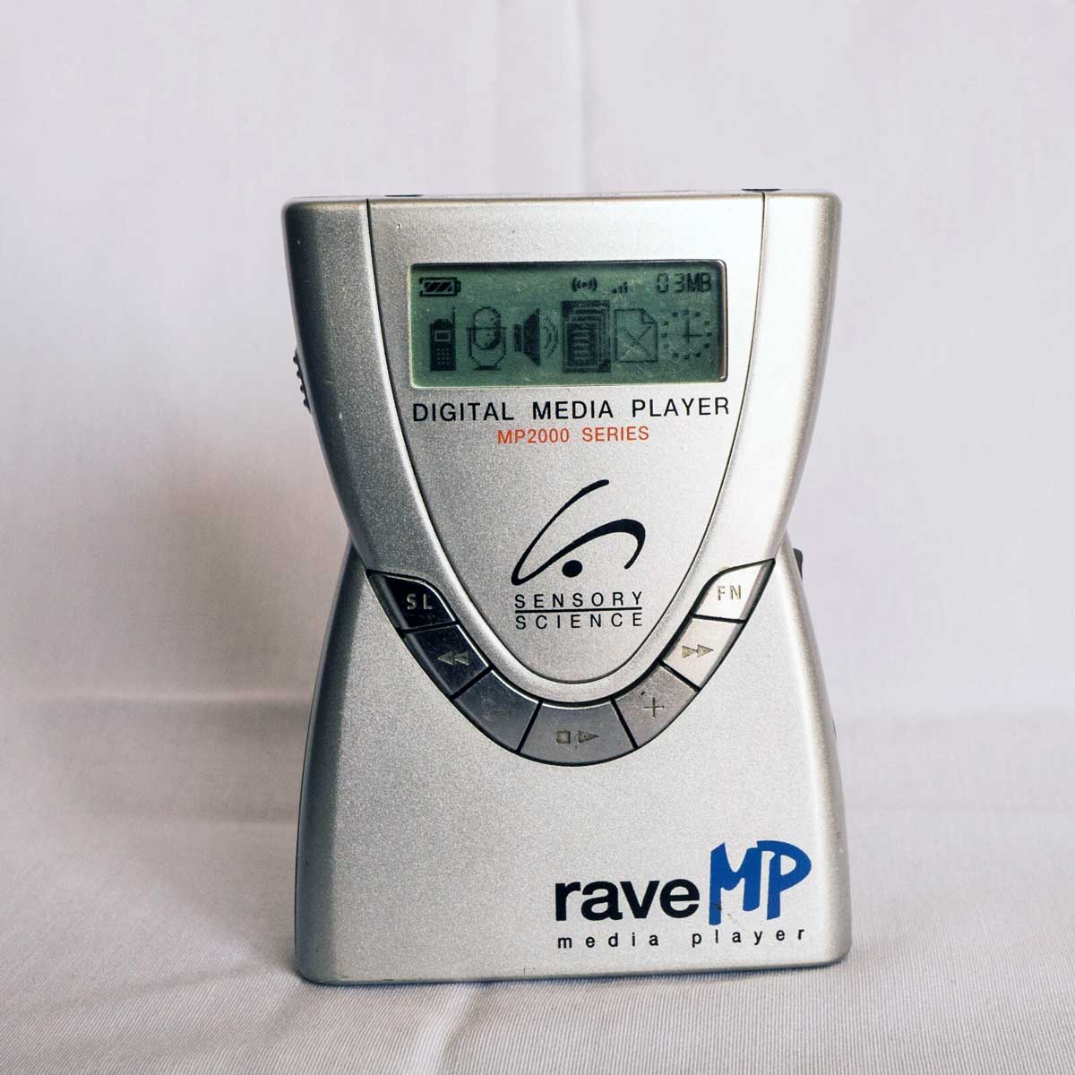 A silver Rave MP MP2000 Series digital media player with a small display screen and control buttons, standing upright on a white surface. The brand “Sensory Science” logo is visible on the front.
