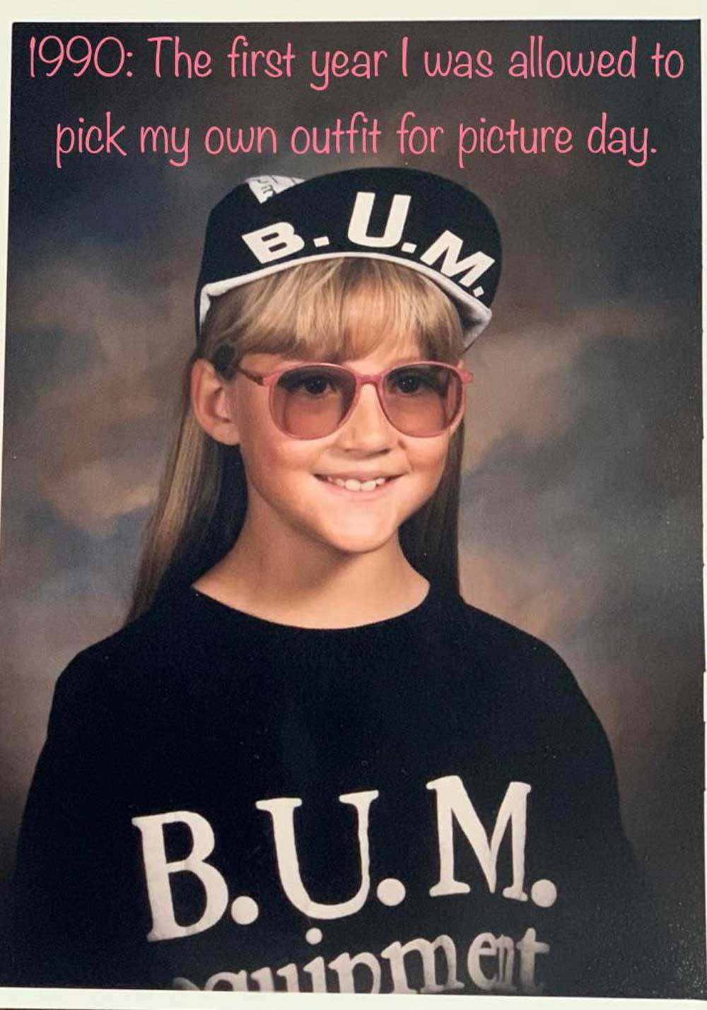 A young girl poses for a school photo wearing a black B.U.M. Equipment shirt, matching hat, and pink sunglasses. The text above her reads, 1990: The first year I was allowed to pick my own outfit for picture day.