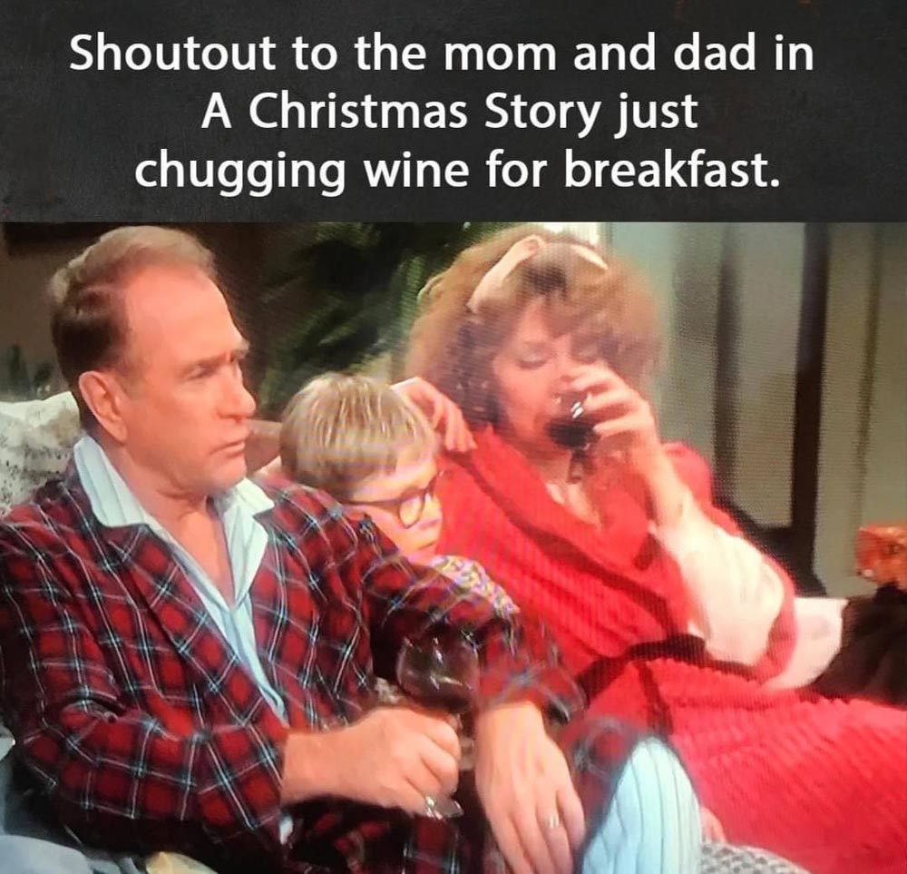 A scene from A Christmas Story shows the parents in robes on a couch with their son. The mom is drinking wine, and the dad holds a glass. Text above reads: Shoutout to the mom and dad in A Christmas Story just chugging wine for breakfast.