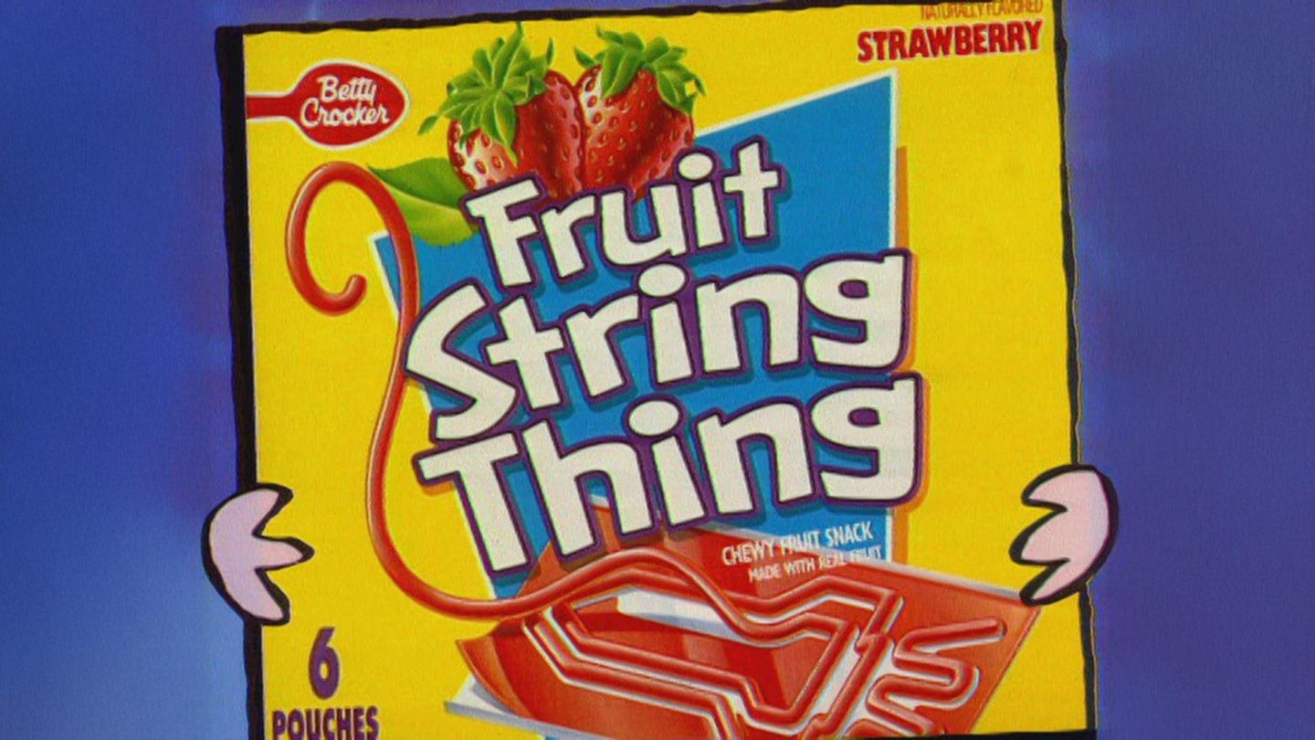 A bright yellow box of Betty Crocker Fruit String Thing, strawberry flavor, with cartoon hands holding it. The box features images of two strawberries and red string-shaped fruit snacks.