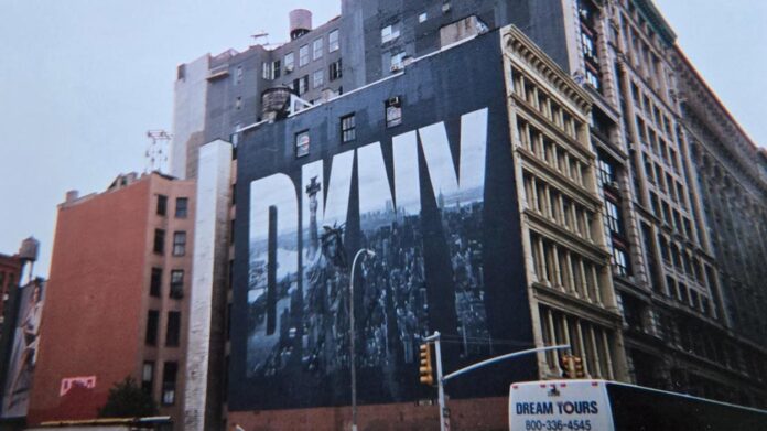 A large city building features a mural with the bold white letters DKNY over a black-and-white photo of the New York City skyline. A Dream Tours bus is visible in the foreground.