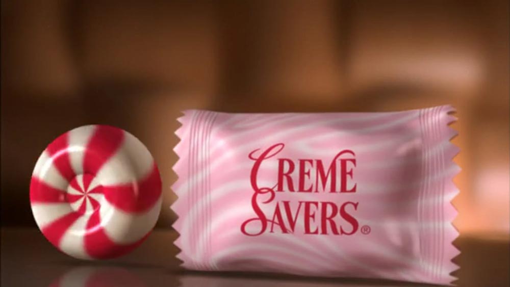 A red and white swirled Creme Savers candy sits next to its pink and white striped wrapper with Creme Savers written in bold red letters.