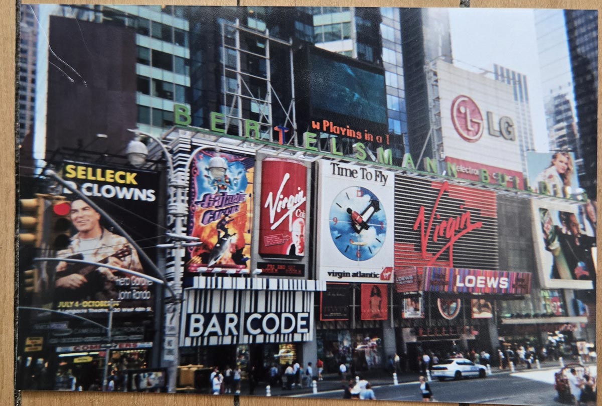 Colorful Times Square scene with large advertisements, including Virgin Atlantic, LG, Loews, a Selleck Clowns show, Jet Fuel Only, and Time To Fly, above a busy street with people and vehicles.