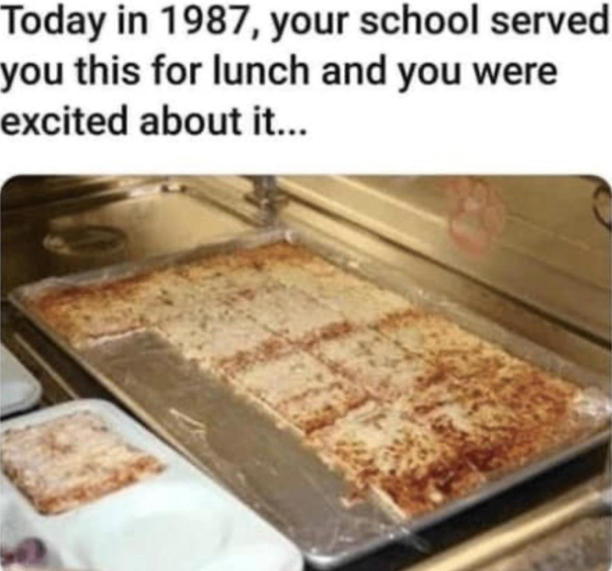 A metal tray holds large rectangular pieces of school cafeteria pizza, cut into squares. Above the tray is text reminiscing about being excited for this lunch in 1987.