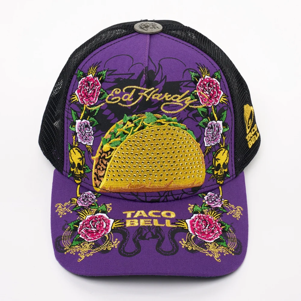A purple and black mesh trucker hat featuring Ed Hardy and Taco Bell logos, with a large embroidered taco, colorful roses, and yellow patterns on the front and brim.